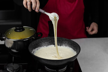 Chef cook making white cheese sauce for mac and cheese meal. Ingredients: Milk, cheese, flour and butter in wok pan on kitchen gas stove.
