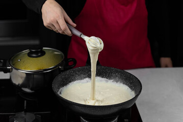 Chef cook making white cheese sauce for mac and cheese meal. Ingredients: Milk, cheese, flour and butter in wok pan on kitchen gas stove.