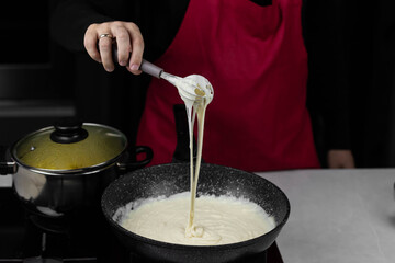 Chef cook making white cheese sauce for mac and cheese meal. Ingredients: Milk, cheese, flour and butter in wok pan on kitchen gas stove.