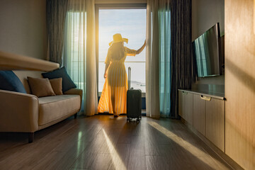 Businesswoman in dress standing with luggage in hotel room, looking magnificent view from hotel...