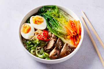 Ramen noodle soup with eggs, mushrooms, pak choi in white bowl