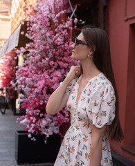 A young woman in an elegant dress strolls past the shops.