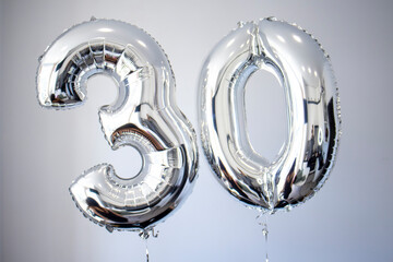 Silver color balloons with numbers 30 anniversary. Figures against a white wall.