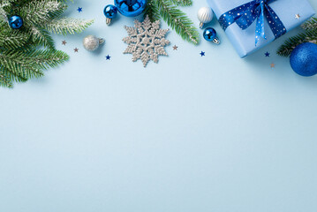 New Year celebration concept. Top view photo of giftbox with bow blue and white baubles snowflake ornament pine branches in snow and confetti on isolated pastel blue background with copyspace