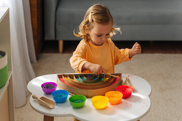 A little girl playing colored rice and make rainbow. Child filled the rainbow with bright rice. Montessori material. Sensory play and learning colors activity for kids.