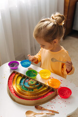 A little girl playing colored rice and make rainbow. Child filled the rainbow with bright rice....