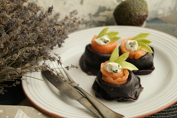 Festive bright appetizer. New Year's table. black pancakes with cuttlefish ink, salmon and avocado. black food. pancake week. Vegetarian pancakes. seafood. Useful lunch. homemade food