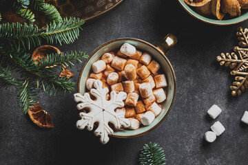 Green cup of hot cocoa with marshmallow decorated with mini gingerbread snowflake.