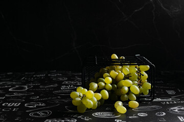 Kishmish grapes in a metal black grid stand, on a black background, in a low key, dark photo