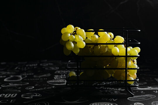 Kishmish grapes in a metal black grid stand, on a black background, in a low key, dark photo