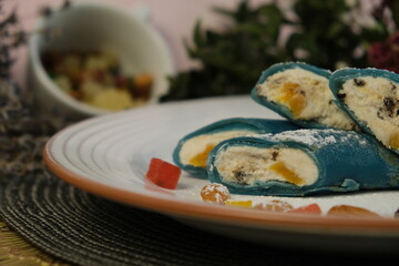 Festive bright dessert. Colored fried pancakes. on a white plate. Turquoise and blue bliny. Stuffed with sweet cottage cheese with dried apricots, prunes, nuts. Delicious stuffing. Maslenitsa