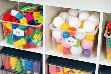 Transparent plastic containers with various children's toys on shelves. Storage box with label...