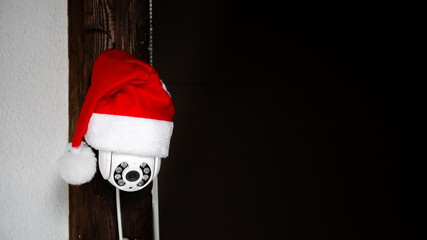 White CCTV camera in red Santa Claus hat. Outdoor video surveillance. Security system. Copy space....