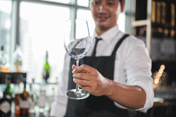 Asia Bartender holding wine glass preparing cocktail with city background at hotel	