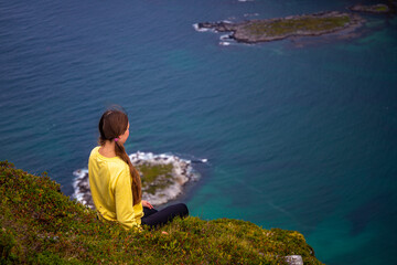 Girl sits on top of Offersøykammen enjoying the panorama of the lofoten islands, Norway; hiking in the Norwegian fjords
