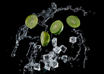 Fototapeta na wymiar Fresh limes, ice cubes and water splashes, isolated on black background