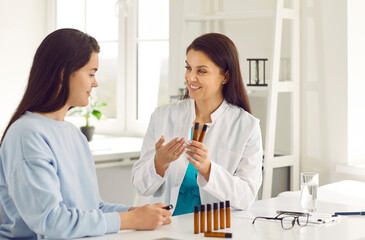 Homeopathy. Friendly female doctor in her office presents to young woman bottles of essential oils to improve well-being. Concept of alternative medicine treatment.