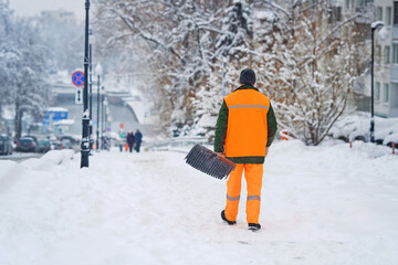 Snow removal work, worker with shove walk on snowy street. Utility worker ready to remove snow. Man...