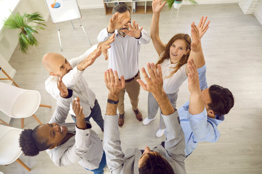 Successful business people on corporate team building training standing with hands up in office with their coach, top view. Seminar is aimed at rallying colleagues and creating effective working team.