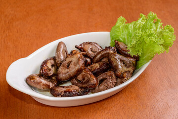 Grilled chicken heart in small white bowl on wooden table. Popular dish in Brazil