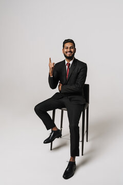 Young indian man pointing finger upward while sitting on chair
