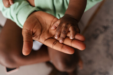 Young african american woman holding her baby's hand at home
