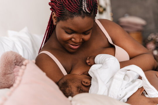 Young african american woman breastfeeding her baby in bedroom