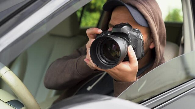 Investigator or private detective, reporter or paparazzi sitting in car and taking photo with professional camera