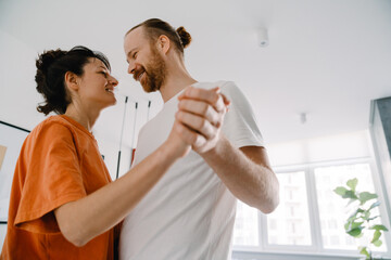 Young white couple smiling and dancing together in bedroom at home