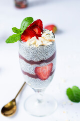 Vegan Chia pudding snack with fresh strawberries and jam served in a tall glass with a fresh mint leaf and coconut flakes for breakfast
