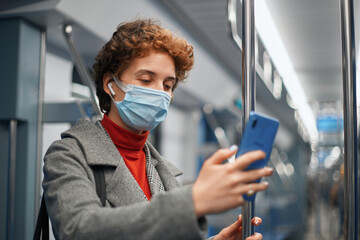 Fototapeta na wymiar young woman in a protective mask taking a selfie while standing in a subway car .