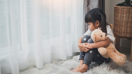 Close up lonely little girl hugging toy, sitting at home alone, upset unhappy child waiting for parents, thinking about problems, bad relationship in family, psychological trauma