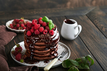 Chocolate Pancakes. Pancakes with fresh raspberry with chocolate glaze or toppings in gray bowl on old wooden table background. Homemade classic american pancakes. Page for magazine concept.