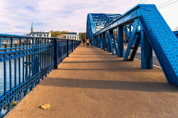 Blue metal bridge over the river, autumn leaf on the pedestrian part of a large metal bridge and...