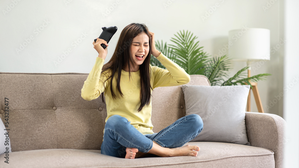 Wall mural young asian woman is using video game control joystick to playing games with enjoyment and raising b