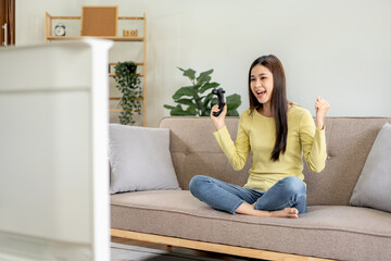Young asian woman is using video game control joystick to playing games with enjoyment and raising both