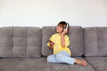 Girl of 8 years old in a yellow t-shirt and blue jeans with phone and headphones.