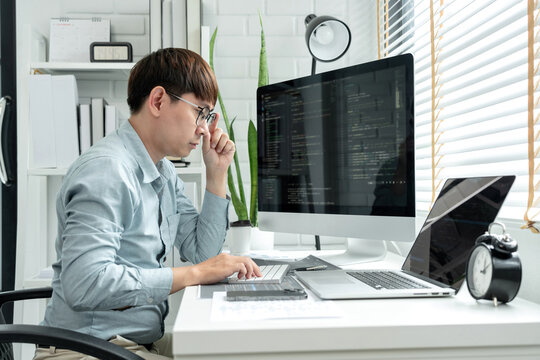 Male programmer is programming to develop program app and website of corporate while working to checking program code and debugging on multiple screen at modern software office