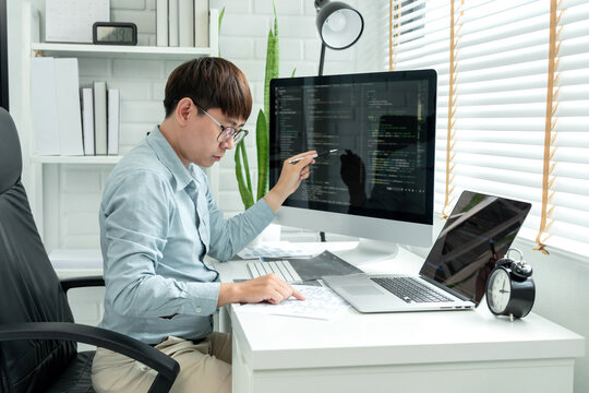 Male programmer is programming to develop program app and website of corporate while working to checking program code and debugging on multiple screen at modern software office