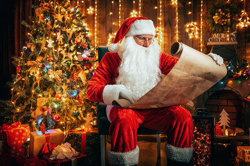 Obraz na płótnie Canvas Santa Claus sitting in room decorated for Christmas, and read the wish list of good boys and girls.