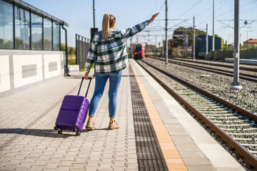 Woman with suitcase waving to a train on station.
