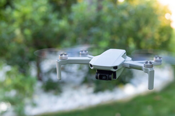 Close up view of small drone flying being controlled by human from remote control in green nature blurred background