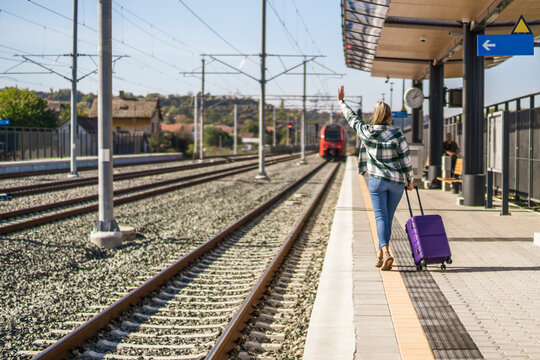 Woman waving  to a leaving train and running  along station with suitcase.