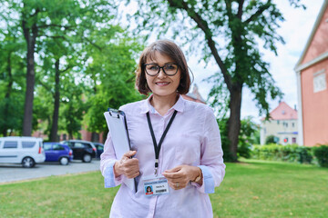 Female educator with clipboard, card of education center looking at camera