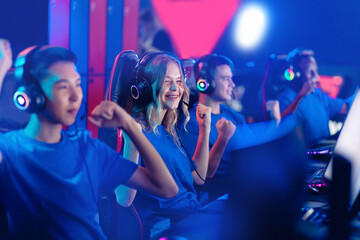 Winner cyber team, young caucasian woman pro gamer with multi-racial group playing in online video game, neon color soft focus - obrazy, fototapety, plakaty