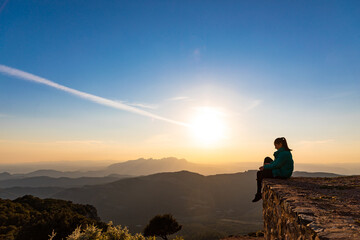 Beautiful woman sitting on an edge during sunset with mountains