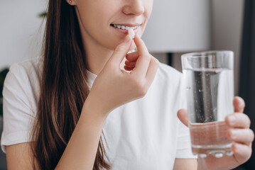 Healthy lifestyle concept. Close up of smiling attractive woman holding round pill and glass of water, happy young caucasian female taking supplement, daily vitamins for hair and skin, natural beauty