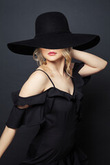 Young perfect woman wearing black dress and black wide broad brim hat  against black background