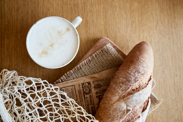 Fresh crust baguette with cappuccino on newspaper wooden table. French traditional morning