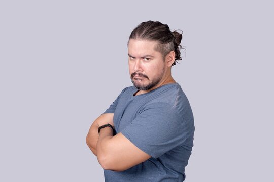 A bitter man in his 30s looking at the camera with a scowling face and arms crossed. Jealousy, displeasure or pettiness.